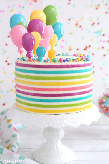 Striped Buttercream Balloon Cake on a white cake stand in front of a polka dot background.