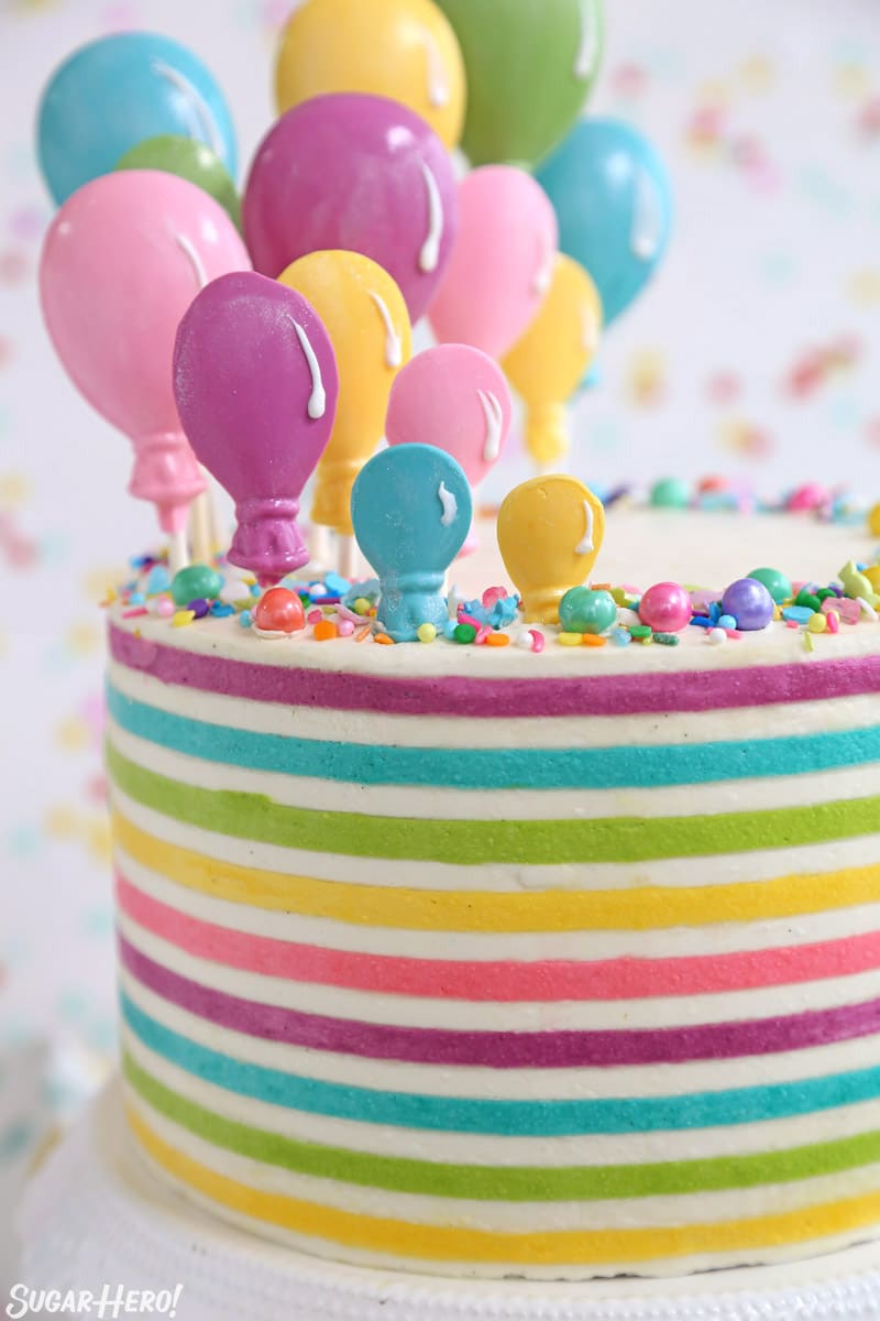 Striped Buttercream Balloon Cake on a white cake stand in front of a polka dot background.
