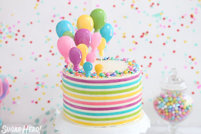 Striped Buttercream Balloon Cake on a white cake stand in front of a polka dot background.