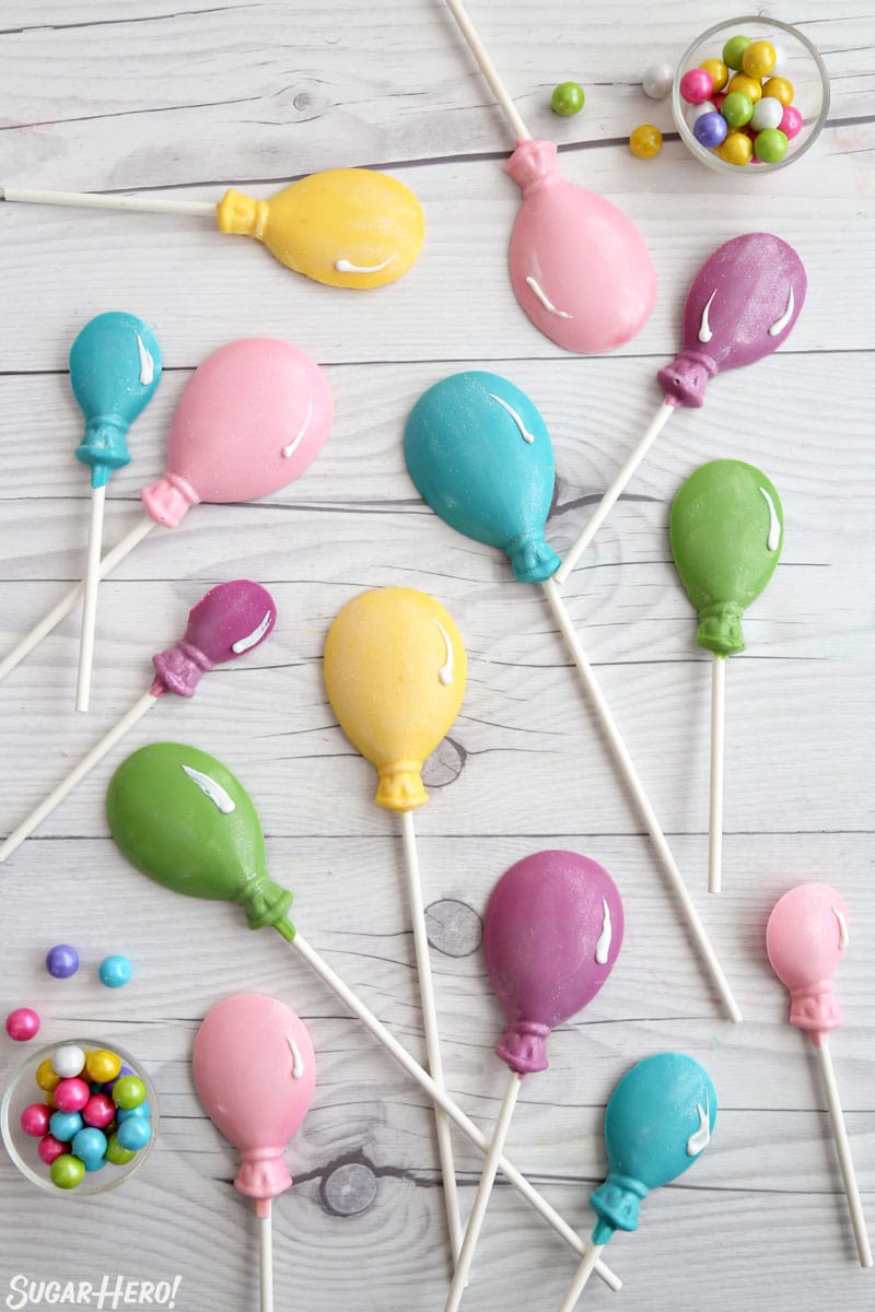 Overhead shot of colorful balloon lollipops on white wooden surface.