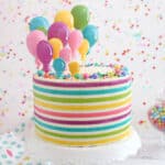 Striped Buttercream Balloon Cake on a white cake stand in front of a polka dot background.