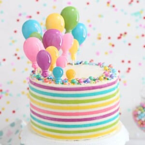 Striped Buttercream Balloon Cake on a white cake stand in front of a polka dot background.