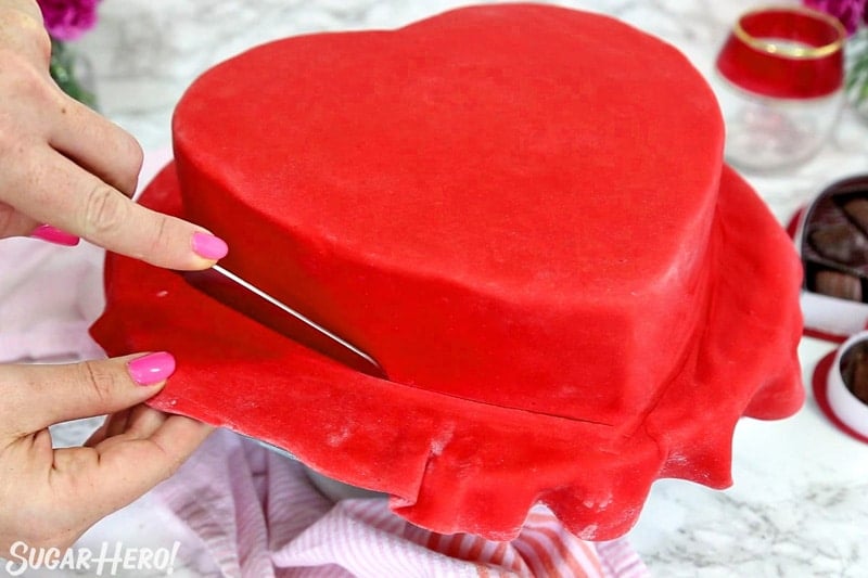 Box of Chocolates Cake - cutting the excess red fondant from the base of the cake | From SugarHero.com