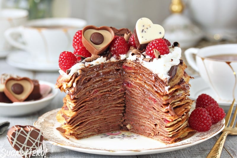 These Chocolate Raspberry Mini Crepe Cakes are so beautiful and elegant! Miniature crepes are layered with chocolate and fresh raspberries to make a unique and delicious dessert. | From SugarHero.com Chocolate Raspberry Mini Crepe Cakes - A crepe cake with a slice taken out. | From SugarHero.com