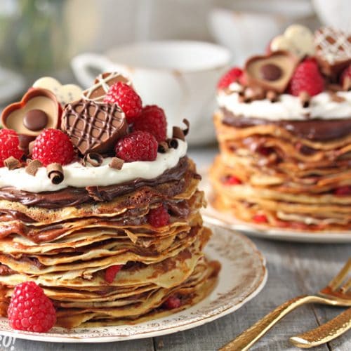 2 Chocolate Raspberry Mini Crepe Cakes on gold edged plates next to gold forks.