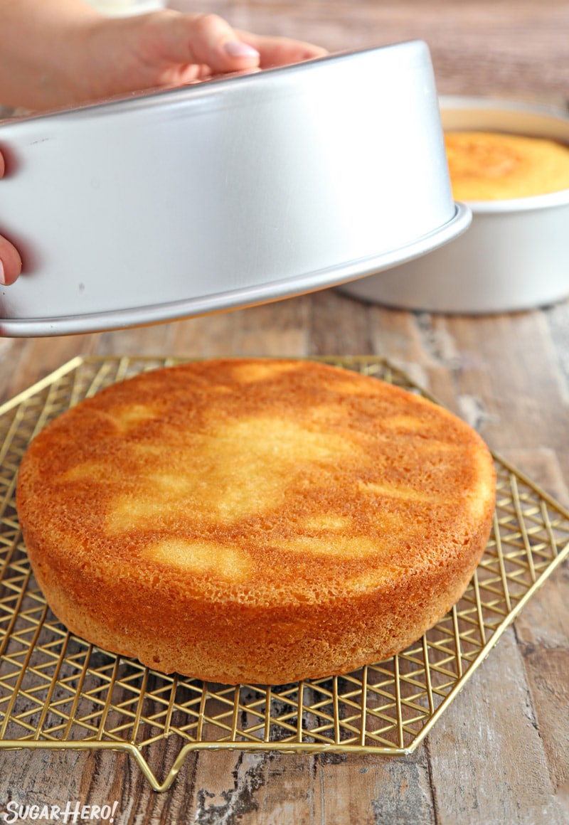 Yellow cake being turned out of a silver cake pan onto a gold cooling rack