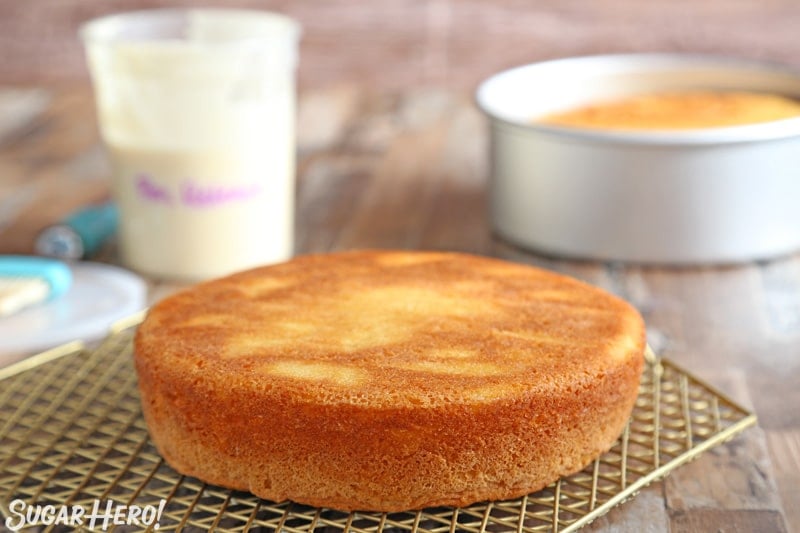 Yellow cake cooling on a gold cooling rack with a container of pan release in the background