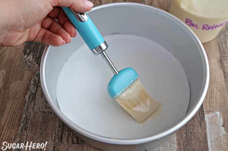 Teal pastry brush brushing homemade pan release on the bottom of a silver cake pan