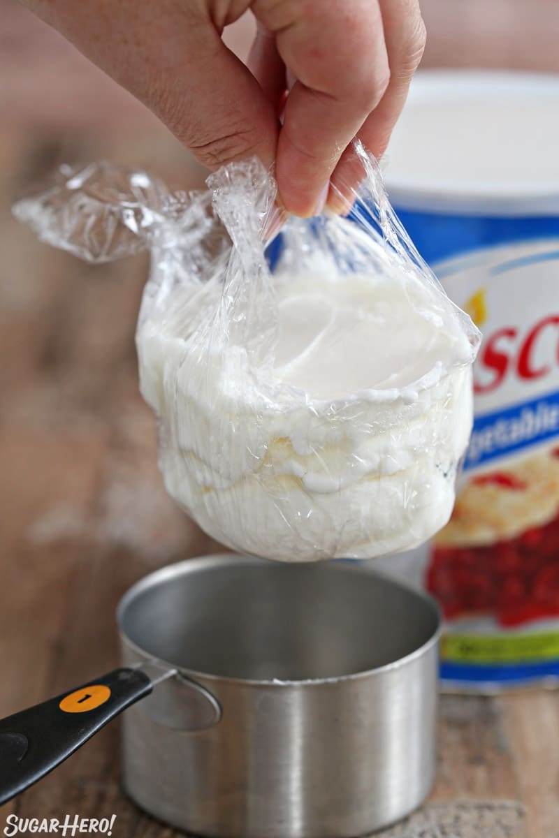 How to Measure Shortening - Tips and Tricks for Measuring Shortening Easily | From SugarHero.com Lifting shortening from a metal measuring cup using plastic wrap