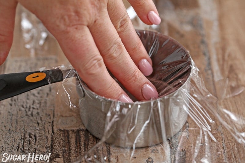 Pressing plastic wrap into the inside of a metal measuring cup