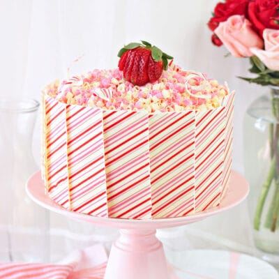 Strawberries and Cream Layer Cake on a pink cake stand with roses in the background.