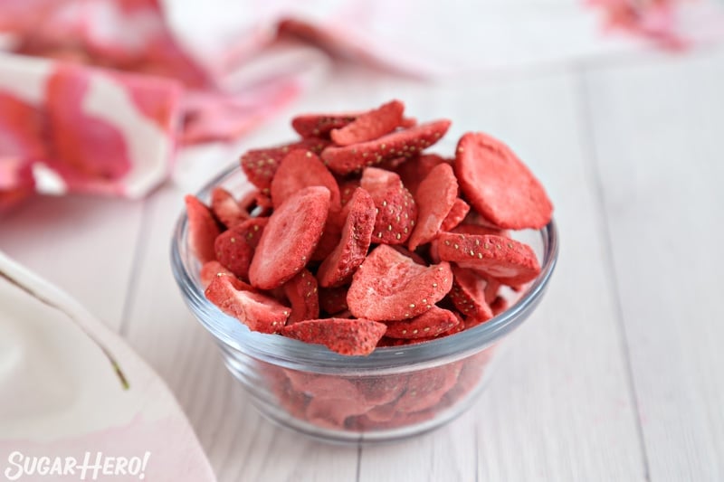 Strawberry Buttercream Frosting - bowl of freeze-dried strawberries on white wood background | From SugarHero.com