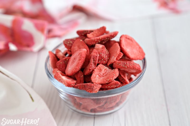This Strawberry Buttercream is incredible! With a smooth, creamy texture and bright fresh strawberry flavor, it's going to be your new favorite frosting to put on everything! | From SugarHero.com Strawberry Buttercream Frosting - bowl of freeze-dried strawberries on white wood background | From SugarHero.com