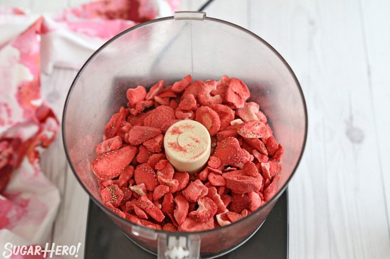 This Strawberry Buttercream is incredible! With a smooth, creamy texture and bright fresh strawberry flavor, it's going to be your new favorite frosting to put on everything! | From SugarHero.com Strawberry Buttercream Frosting - freeze-dried strawberries in bowl of food processor | From SugarHero.com