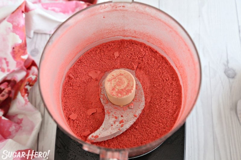 This Strawberry Buttercream is incredible! With a smooth, creamy texture and bright fresh strawberry flavor, it's going to be your new favorite frosting to put on everything! | From SugarHero.com Strawberry Buttercream Frosting - powdered freeze-dried strawberries in bowl of food processor | From SugarHero.com