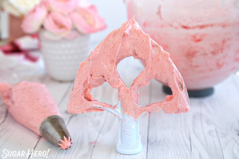 Strawberry Buttercream Frosting - paddle covered in strawberry buttercream with piping bag of frosting next to it | From SugarHero.com