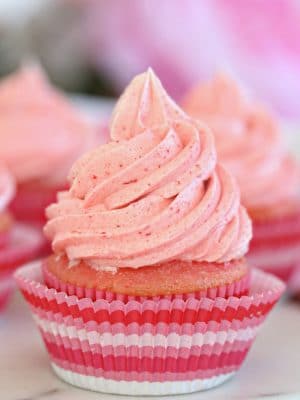 Close up of cupcake frosted with strawberry buttercream in a pink cupcake liner.