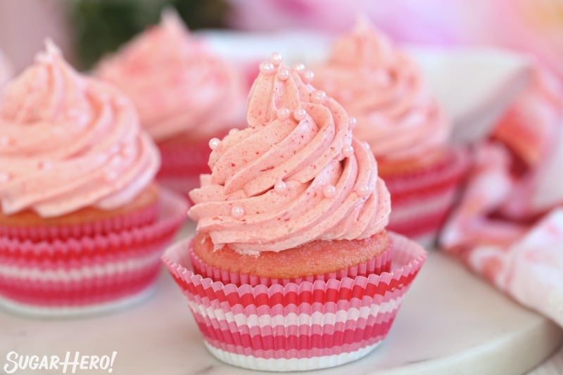 This Strawberry Buttercream is incredible! With a smooth, creamy texture and bright fresh strawberry flavor, it's going to be your new favorite frosting to put on everything! | From SugarHero.com Strawberry Buttercream Frosting - pink cupcakes with strawberry frosting and pink sugar pearls on top | From SugarHero.com