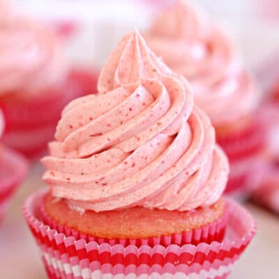 Close up of cupcake frosted with strawberry buttercream in a pink cupcake liner.