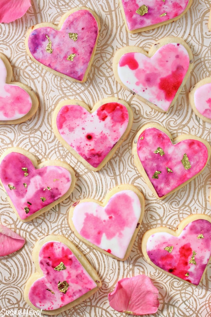 Watercolor Rose Sugar Cookies - Multiple sugar cookies displayed with rose petals. | From SugarHero.com 