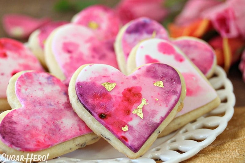 Watercolor Rose Sugar Cookies - Multiple sugar cookies decorated with pink and purple watercolor designs. | From SugarHero.com 