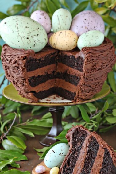 Easter Nest Cake with a slice cut out and set beside it. Greenery in the background of the photo.