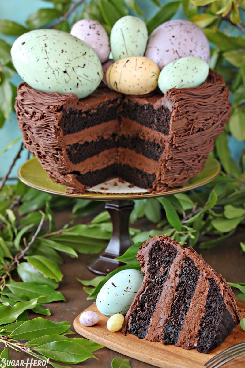 Easter Nest Cake with a slice cut out and set beside it. Greenery in the background of the photo.