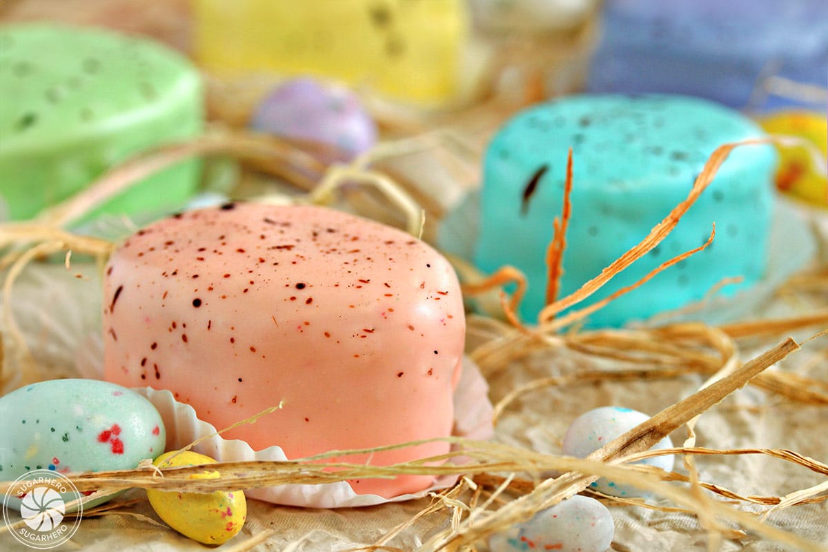 Looking for a gorgeous Easter dessert? Try these Easter Egg Petit Fours! They're sweet mini cakes with a pretty pastel speckled glaze | From SugarHero.com Easter Egg Petit Fours - close-up of speckled pink petit four | From SugarHero.com