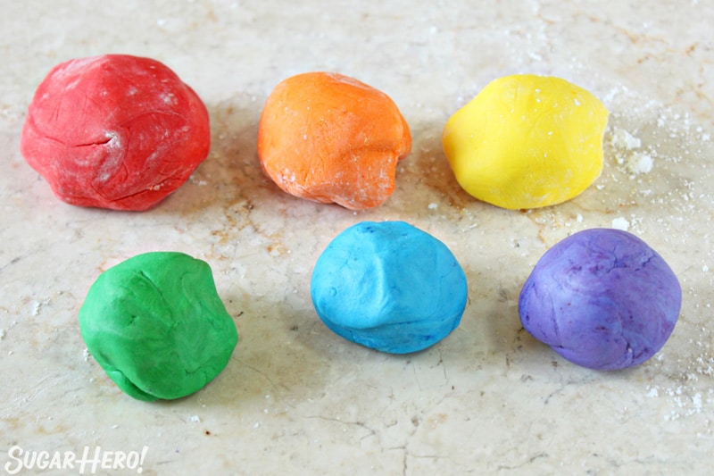 Six balls of colorful fondant on a beige marble surface. 