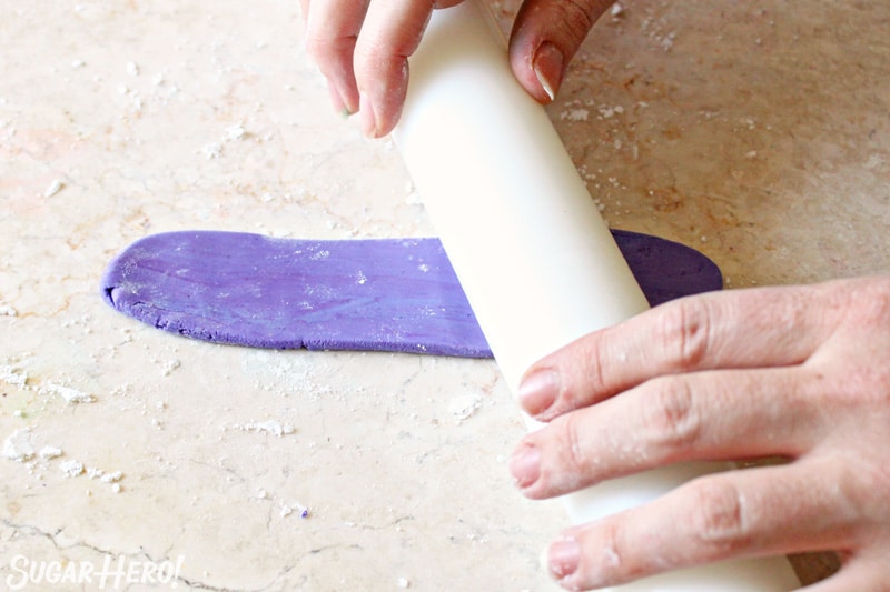 Rolling out a strip of purple fondant with a white fondant rolling pin