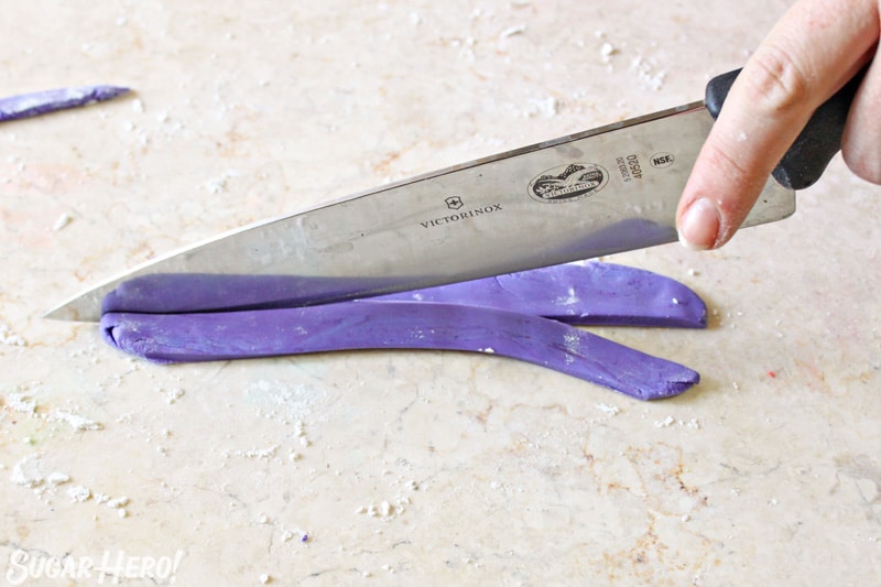 Cutting a strip of purple fondant with a chef's knife
