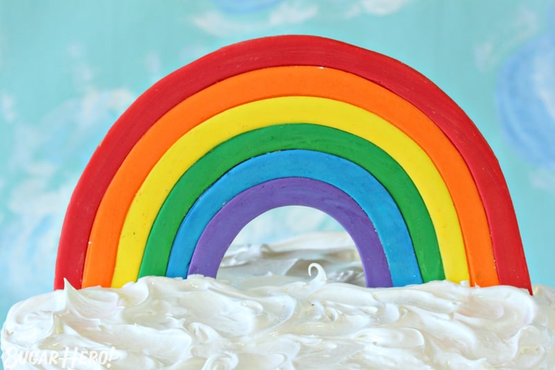 Fondant Rainbow Cake Topper on top of a cake with fluffy white frosting.