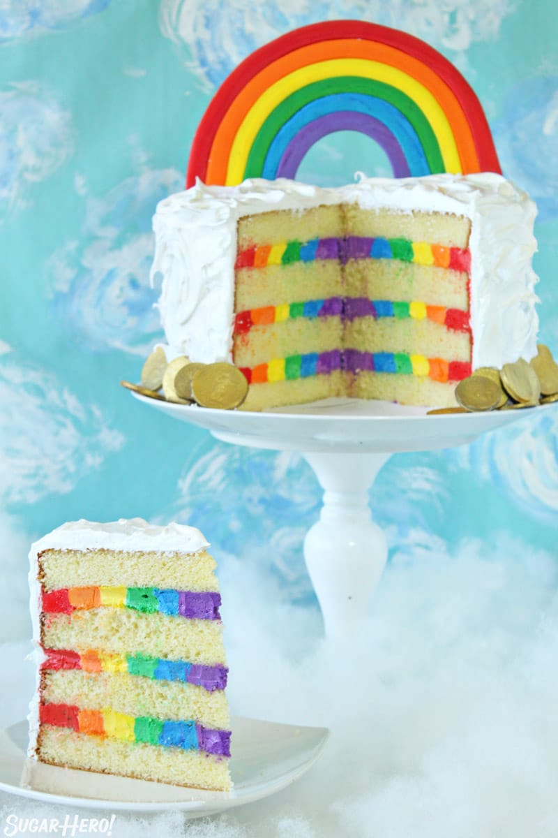 Rainbow cake on a white cake stand with a slice removed