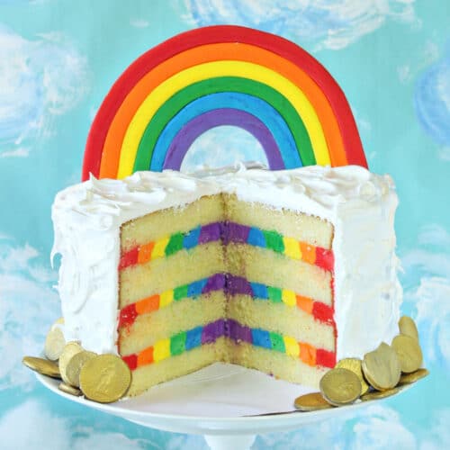 Rainbow cake with a rainbow cake topper, cut open to reveal stripes of rainbow buttercream inside.