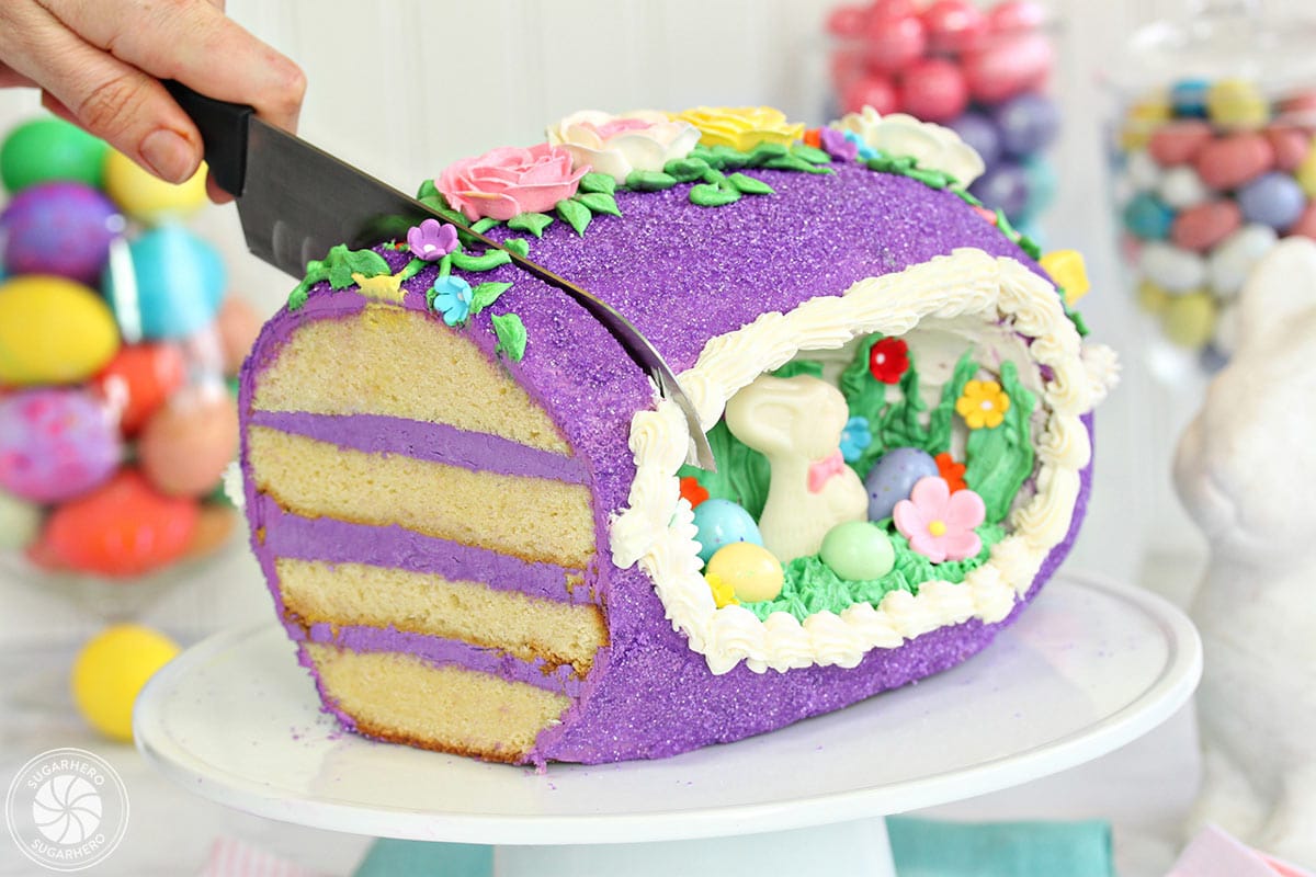 Slicing a sugar easter egg cake on a white cake stand