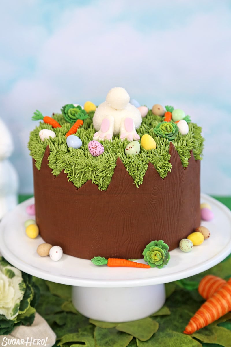 Chocolate Easter Bunny Cake on a white cake stand with fondant decorations and chocolate eggs around the base