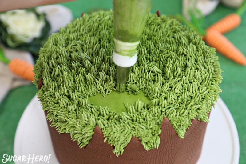 Piping green buttercream onto the top of the cake with a grass piping tip