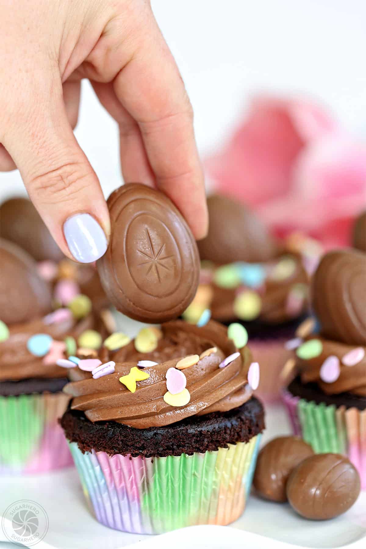 Hand with purple fingernail placing a chocolate egg on top of a chocolate cupcake
