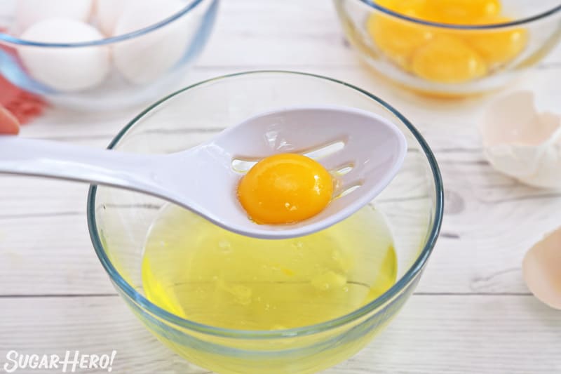 Using a white slotted spoon to separate an egg yolk from an egg white