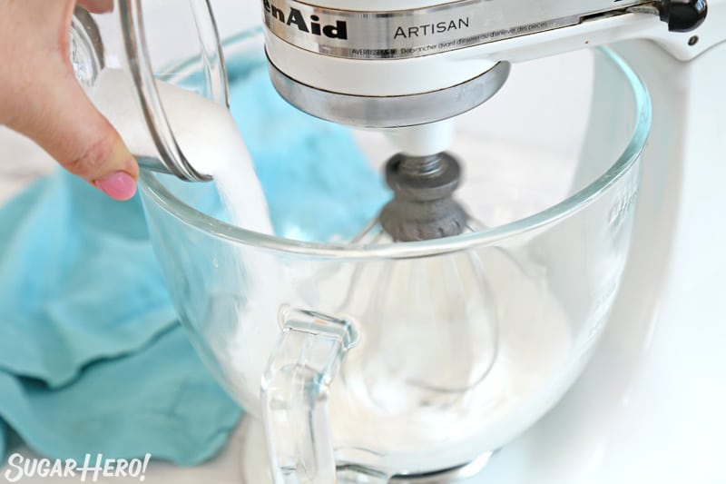 Adding granulated sugar to meringue mixture in glass mixing bowl
