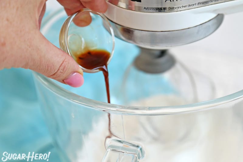 Adding vanilla extract to meringue mixture in glass mixing bowl