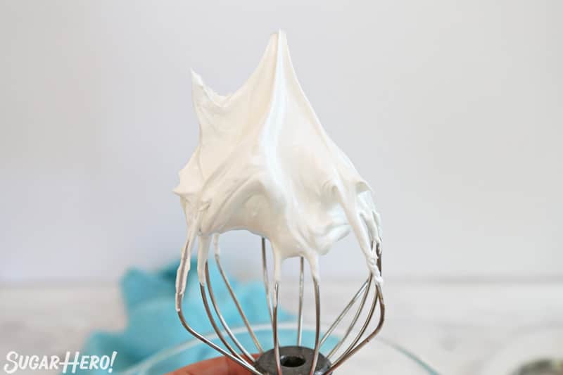 Whisk attachment with meringue mixture showing meringue with stiff peaks