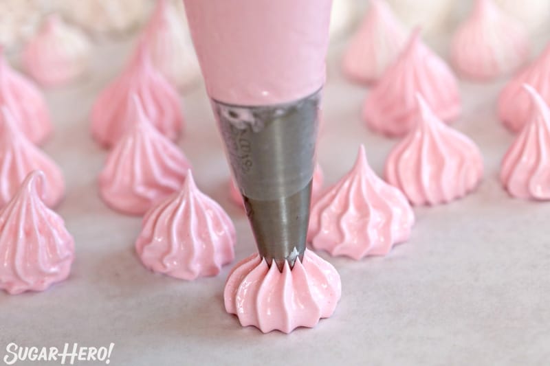 How to Make Meringue Cookies - crispy, crunchy egg white cookies that are fat-free and easy to make! | From SugarHero.com Piping pink meringue kisses on a parchment-covered baking sheet with a large star tip