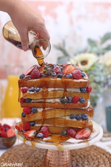 French Toast Cake on a cake stand dripping thick maple syrup while a hand pours it from above.