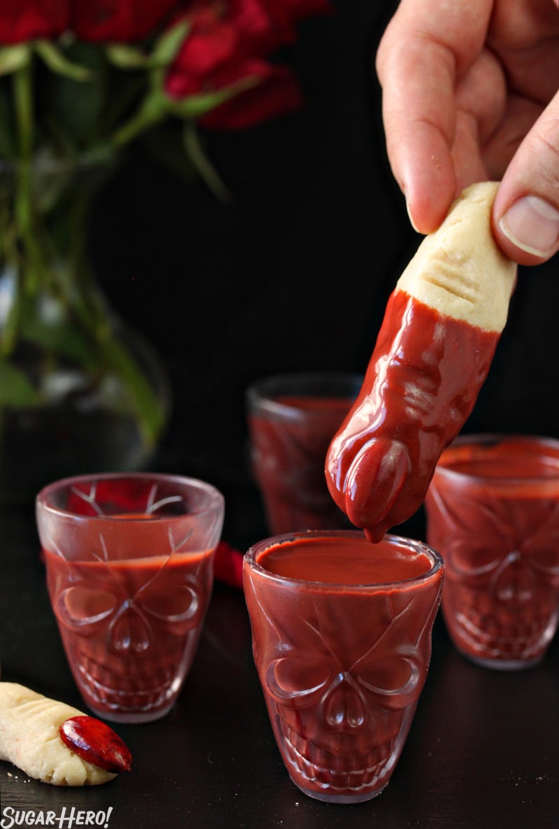 This Red Velvet Hot Chocolate - A shot of a witch finger cookie being dipped into the hot chocolate. | From SugarHero.com