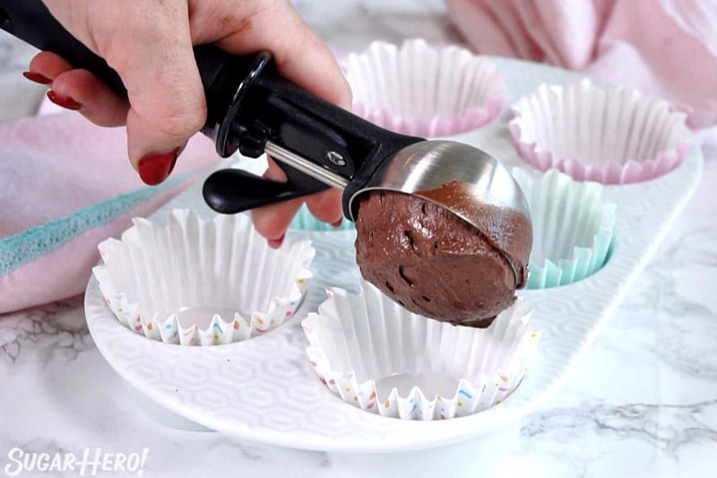 Scooping chocolate cupcake batter into a cupcake pan lined with paper liners