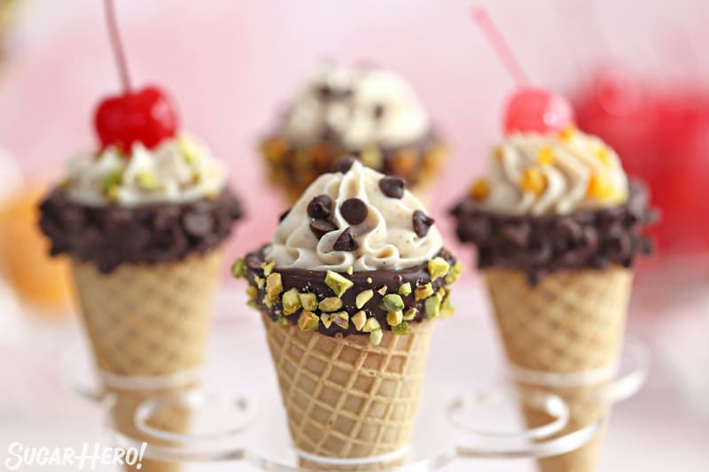 Four cannoli cones topped with chocolate chips, pistachios, nuts, and cherries.