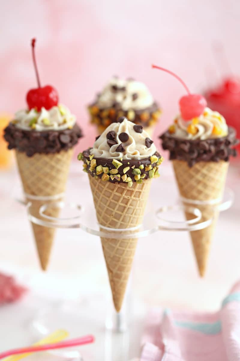 Four cannoli cones topped with chocolate chips, pistachios, nuts, and cherries.