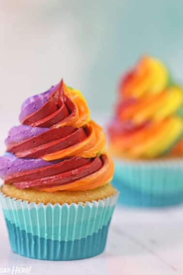 Two cupcakes with tall swirls of colorful rainbow frosting