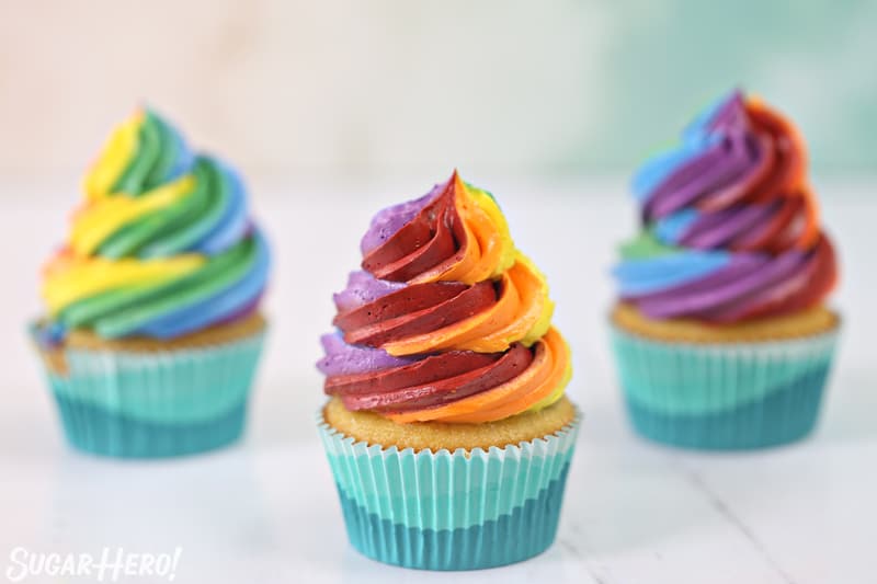 Three cupcakes with colorful rainbow frosting swirls